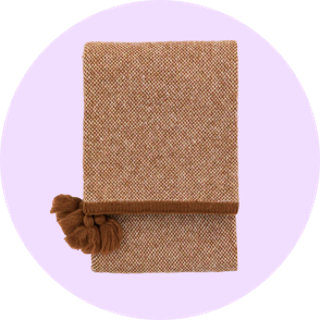 Tan woven throw blanket with tassels on lilac background