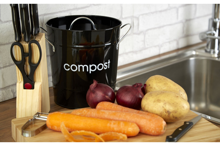 black kitchen counter compost bin next to a range of peeled vegetable skins and scraps