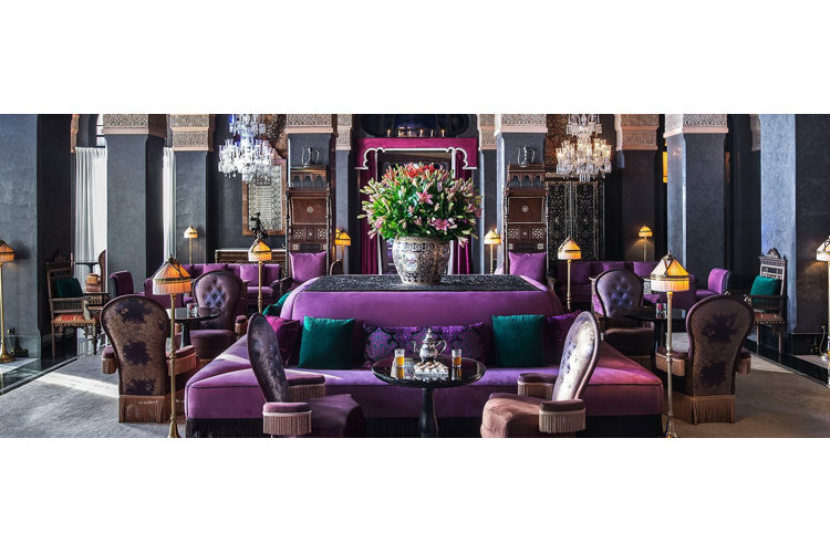 A living room with furniture in varying shades of deep purple. Golden metallic accents, including lamps, and a crystal chandelier.