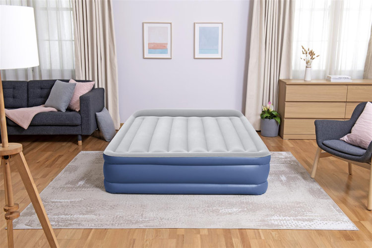 A living room with a gray and blue air mattress on top of a gray rug to create a makeshift sleeping area.