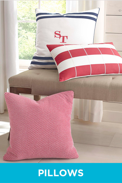 Decorative throw pillows featuring red and white patterns and a monogrammed nautical design arranged on and in front of an upholstered bench, labeled Pillows.