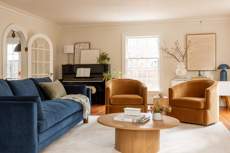 living room layout idea with a blue modern sofa two camel colored accent chairs a round wooden coffee table and a piano in the corner of the room