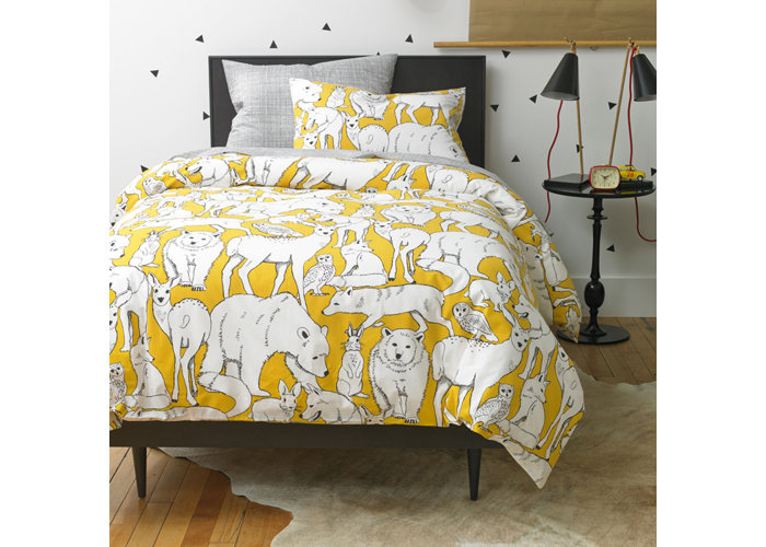 Closeup of a bed with a yellow duvet covered in animals and a back nightstand