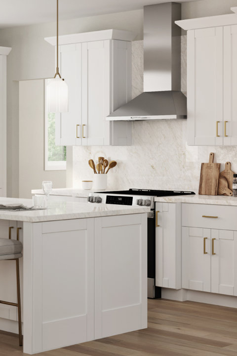 Modern white kitchen with shaker cabinets, gold hardware, marble countertops, stainless steel range hood, and a kitchen island with pendant lighting.