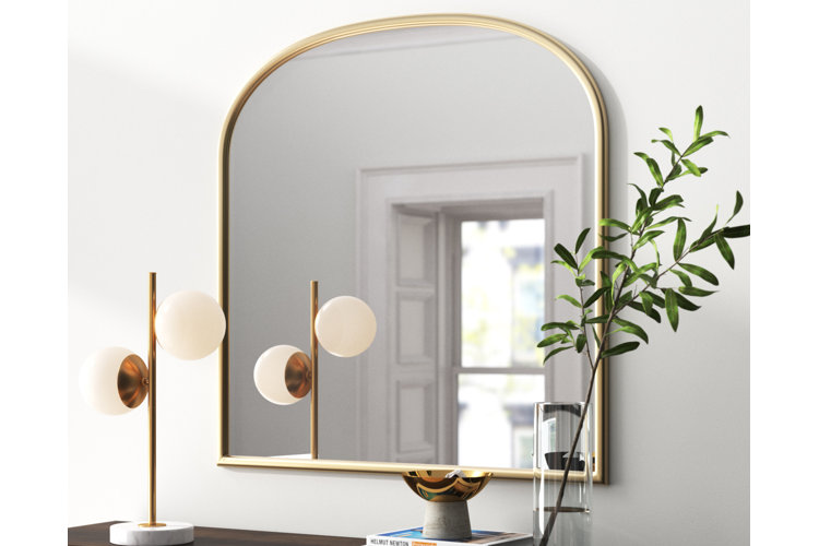 dresser with a gold-framed mirror, modern table lamp, and a vase filled with a leafy branch