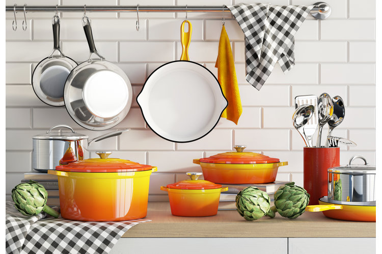 orange cookware set on a wood countertop in front of a white subway tile backsplash