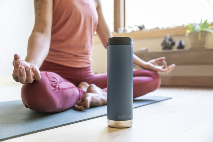A person mediating on a yoga mat with a tumbler in front of them