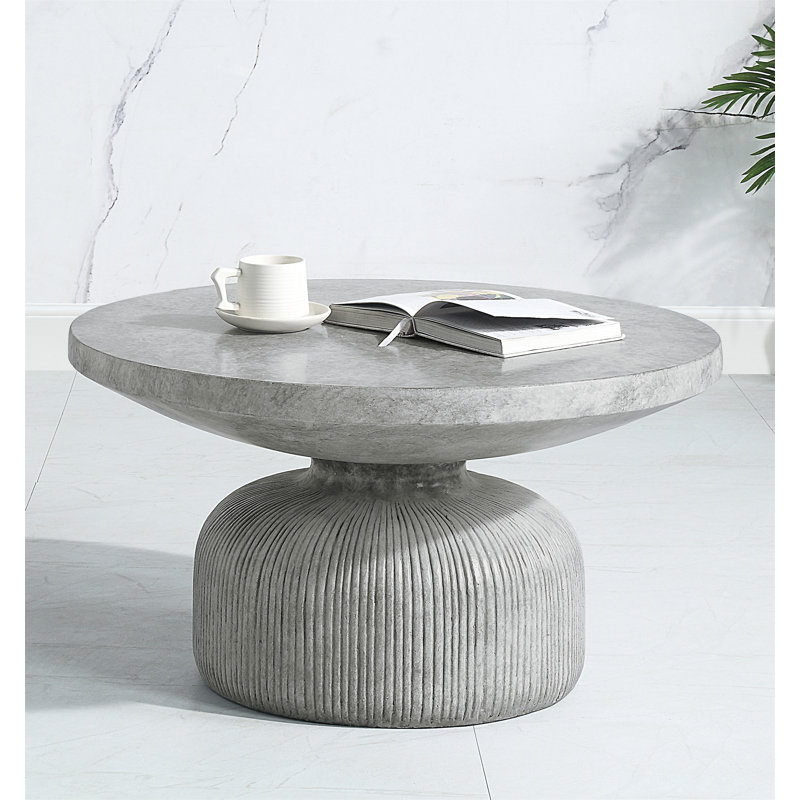 Table basse grise patinée avec plateau rond et base piédestal, parfaite pour les intérieurs modernes et rustiques.