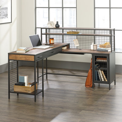 Bureau d'ordinateur industriel en forme de L avec 2 tiroirs et étagères, fini brun, surface de travail spacieuse pour ordinateur portable, bloc-notes, lampe, passe-câbles, étagère réglable derrière une porte métallique.