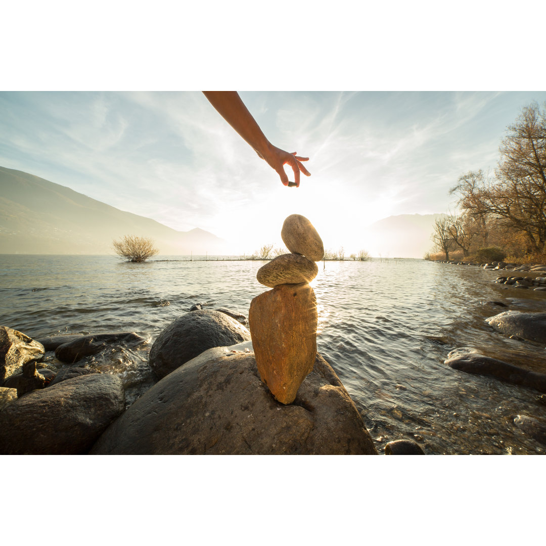 Detail einer Person beim Stapeln von Steinen am See