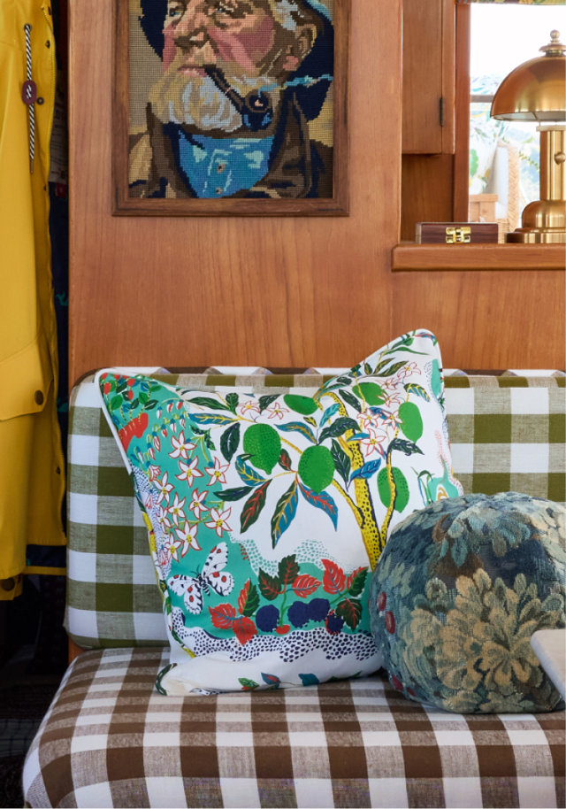Decorative pillows with colorful citrus and floral patterns placed on a green and brown gingham bench seat in a room with wood-paneled walls and vintage decor.