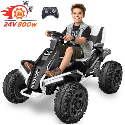 Black and white ride-on go-kart with large treaded tires, LED headlights, and a child driver