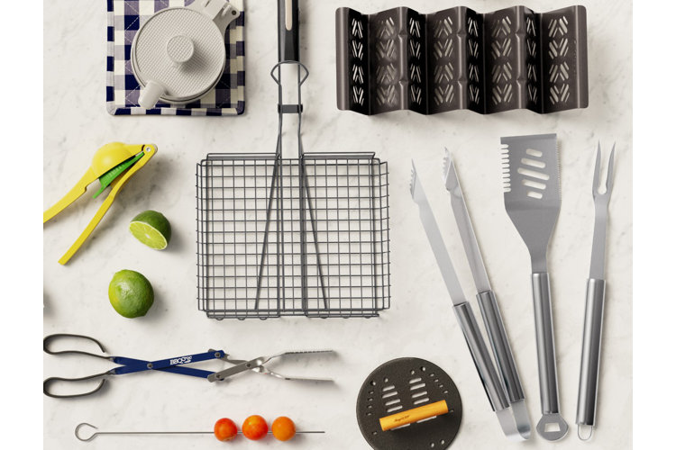 An assortment of grill tools placed on a marble countertop, including baskets, spatulas, skewers, and a burger press.