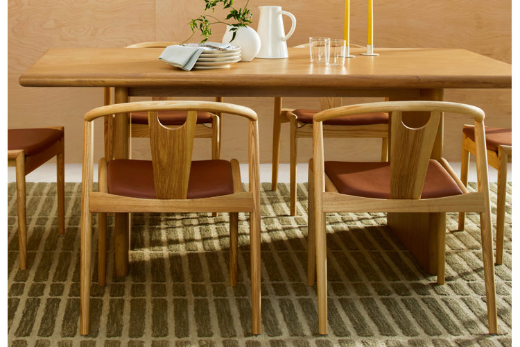 mid-century modern dining room with a wood dining table, matching wood-and-leather dining chairs, green area rug, and simple dinnerware