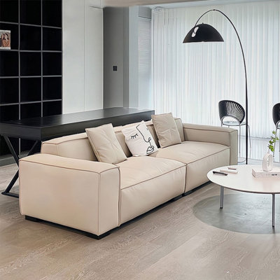 Canapé modulaire en cuir véritable couleur crème avec coussins.