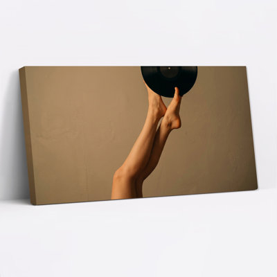Jambes nues tenant un disque vinyle noir sur un mur beige - Tableau sur toile