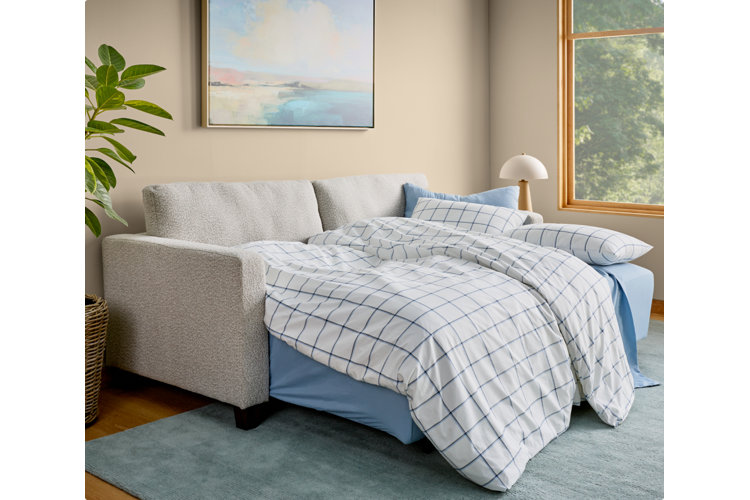 light gray sofa bed with blue sheets, grid-patterned bedding, and a light blue rug