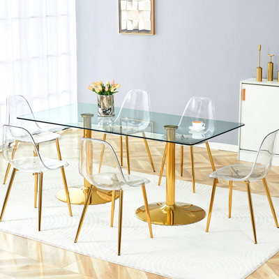 Table à manger moderne et esthétique : plateau en verre trempé de 180 x 90 cm et 6 chaises en plastique transparent avec pattes en métal doré, espace généreux pour les repas en famille.
