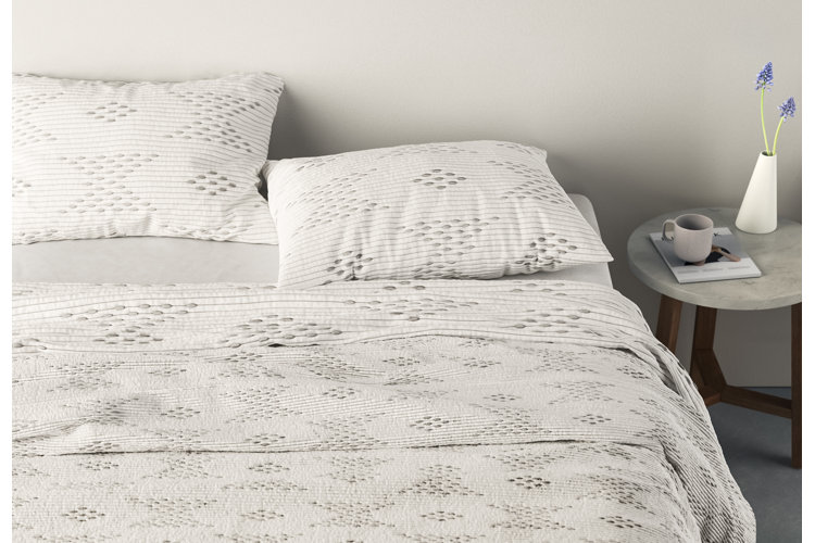 Bed with white, patterned bedding set and a small side table.