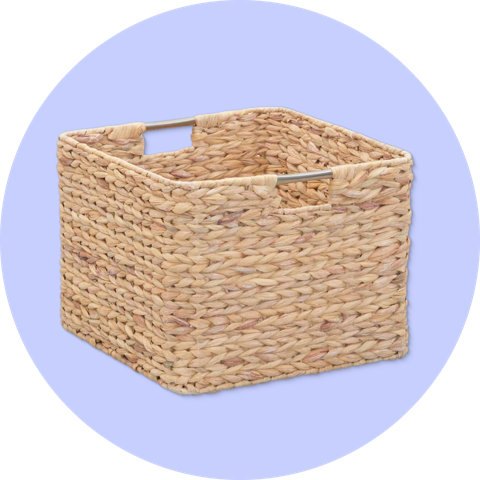 Un panier de rangement en jonc de mer tressé avec des poignées en métal, affiché sur un fond circulaire violet.