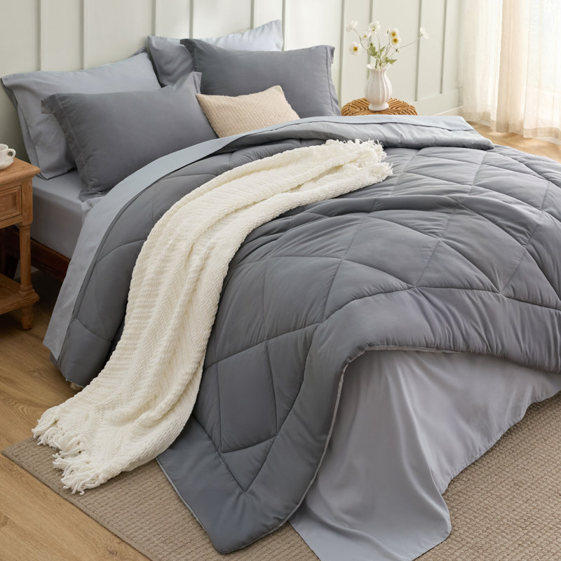 Gray quilted comforter set with diamond stitching and a cream-colored knit throw blanket on a bed.