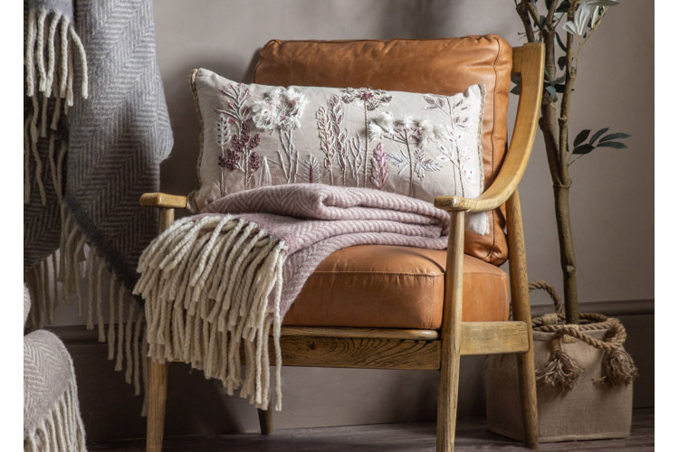 Pink wool blanket with cream and floral pillow on a light brown leather accent chair
