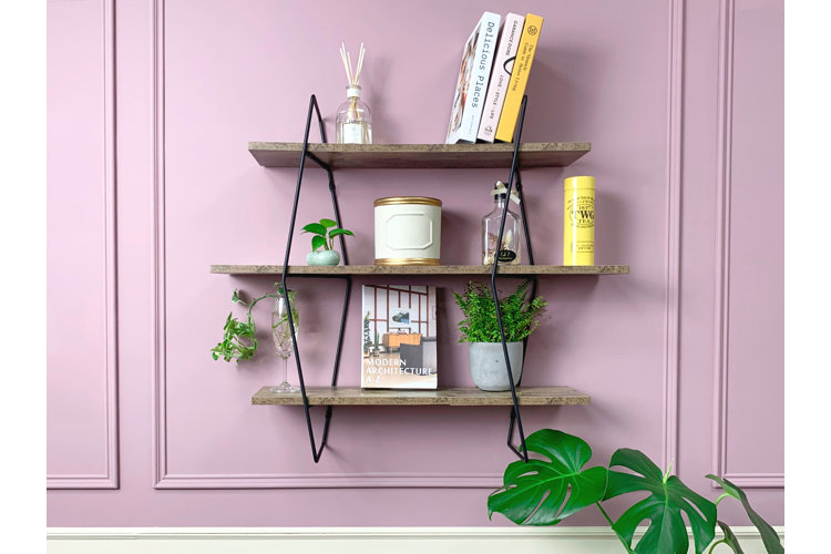 pink wall with a wood and steel tiered shelf filled with home decor