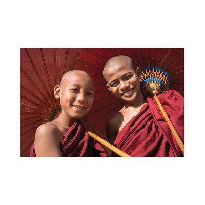 Two Young Buddhist Monks Smiling And Holding Red Umbrellas, Myanmar by Jan Becke - Wrapped Canvas Print