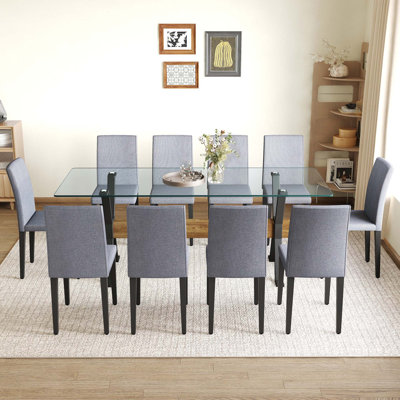 Ensemble de table et de chaises. Plateau de table en verre trempé de 79 po x 31,5 po avec pieds en métal en forme de X, traverse en panneau de fibres à densité moyenne à grain de bois texturé et doublé de chaises en lin et coton.