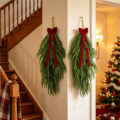 Ensemble de 2 guirlandes de Noël en forme de larme (66 cm) en pin de Norfolk artificiel, avec nœud en velours rouge et clochettes en laiton vintage. Idéal pour décorer les portes, les foyers, les escaliers, les fenêtres et autres espaces extérieurs.