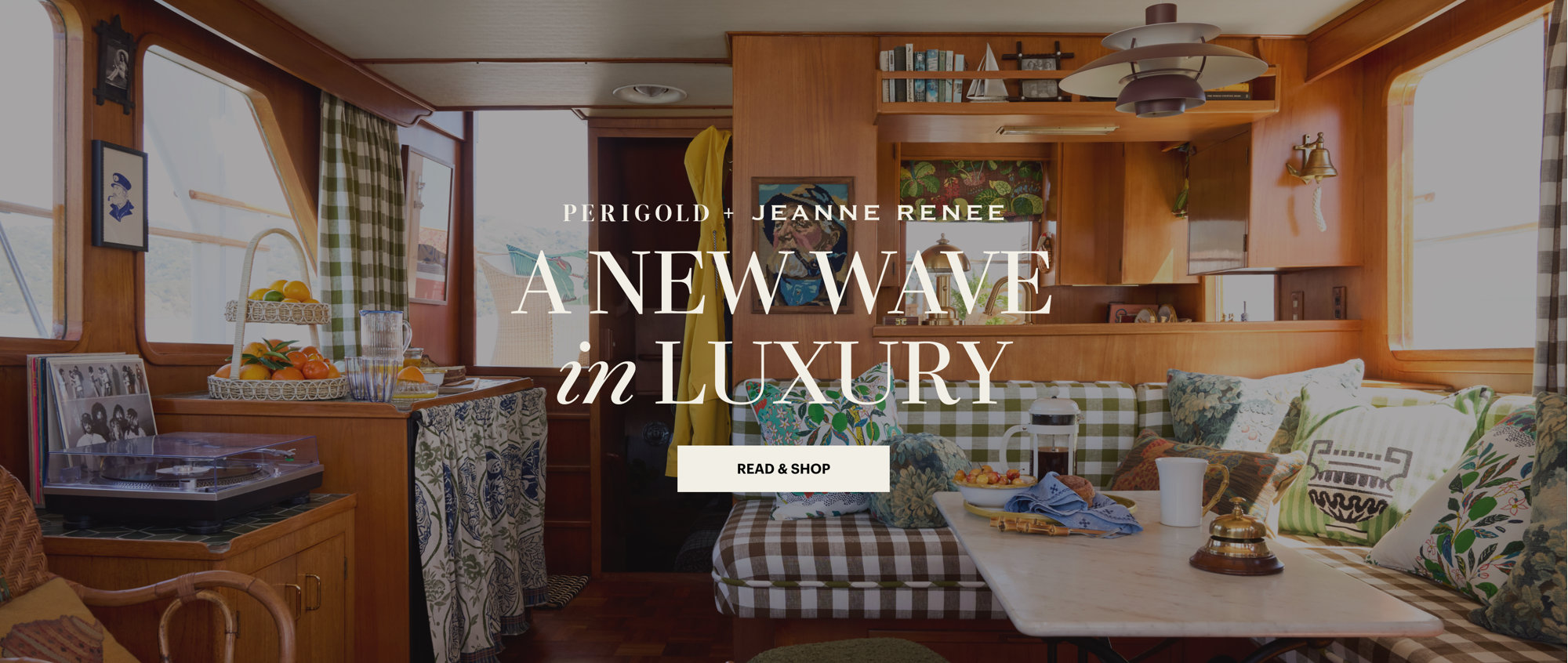 Perigold and Jeanne Renee present A New Wave in Luxury, featuring a cozy wood-paneled interior with a booth seating area, checkered cushions, and decorative accents, with a Read and Shop button.