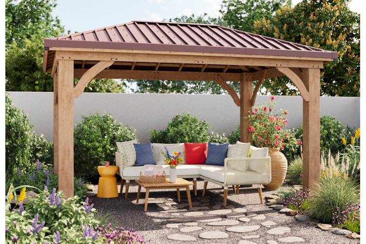 A large wooden gazebo surrounded by plants and used to shade an outdoor seating area with a white patio sectional.
