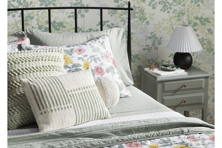 grandmacore bed with striped sheets, floral quilt, and textured throw pillows