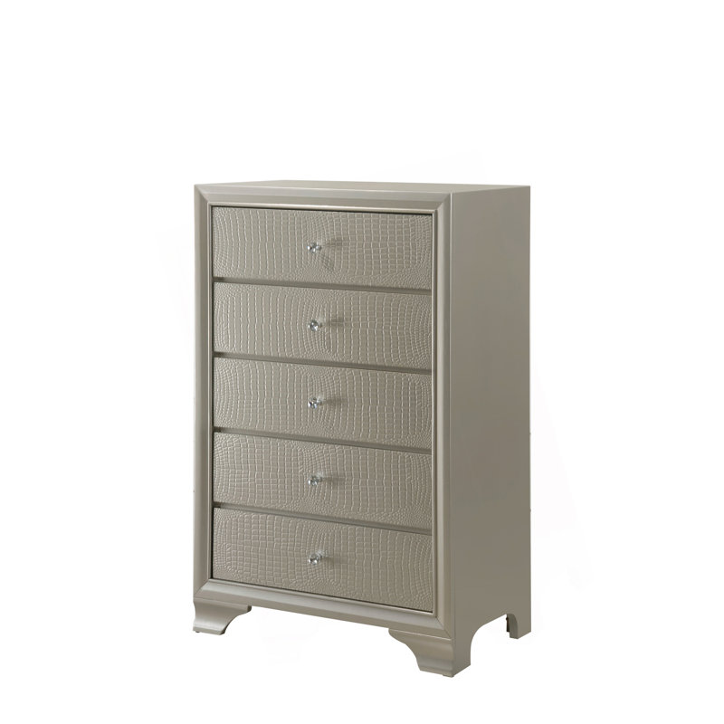 Superbe commode à cinq tiroirs au fini champagne avec des détails glamour pour l'élégance de la chambre à coucher.