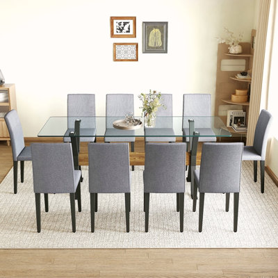 Ensemble de table et de chaises. Plateau de table en verre trempé de 79 po x 31,5 po avec pieds en métal noir en forme de X, traverse en panneau de fibres à densité moyenne à grain de bois texturé et doublé de chaises en lin et coton gris clair.