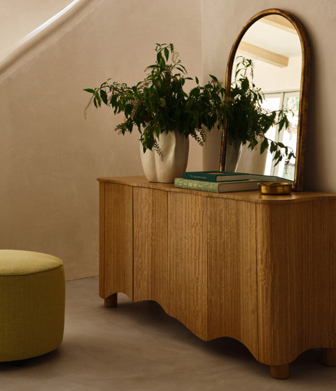 Light wooden cabinet with books titled The Japanese Garden, a vase with flowers, and a mirror.