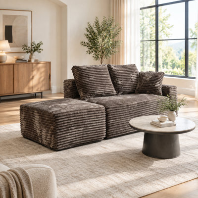 Petit canapé d'angle modulaire Cloud avec assise profonde, pouf et 3 coussins, en velours côtelé marron, méridienne à droite.