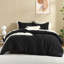 Comforter set in black with cream accent pillow shams, a decorative cream tassel pillow, and a white throw blanket.