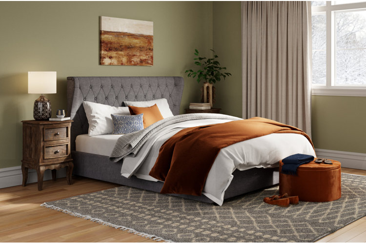 traditional bedroom with olive green walls, a gray upholstered bed, and terracotta bedding
