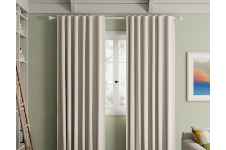 Close up of a window with a pair of beige curtains pushed slightly apart on a white curtain rod.