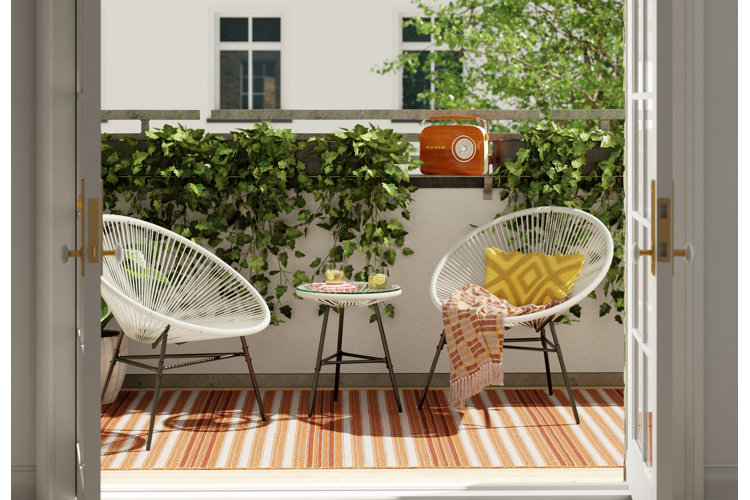 Apartment balcony with a wicker chair set and striped outdoor rug demonstrating compact outdoor seating for small spaces