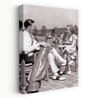 1930s COUPLE MAN AND WOMAN SITTING ON PATIO EACH WITH GOLF BAG AND CLUBS TALKING ABOUT THE GAME DRESSED IN SUMMER CLOTHES by H. Armstrong Roberts - Wrapped Canvas Print