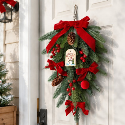 Décoration murale artificielle de Noël en forme de larme (60 cm), ornée de nœuds en velours rouge, de baies, de pommes de pin et d'une étiquette bonhomme de neige, idéale pour décorer votre porte d'entrée pendant les fêtes.