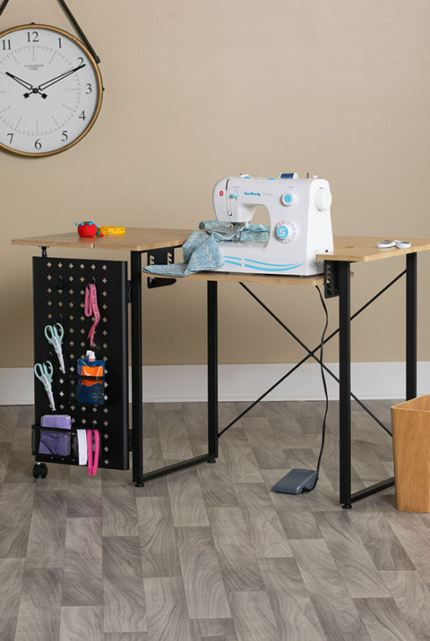 Light wood sewing desk featuring a side pegboard panel with craft storage hooks and a sewing machine set up on top.