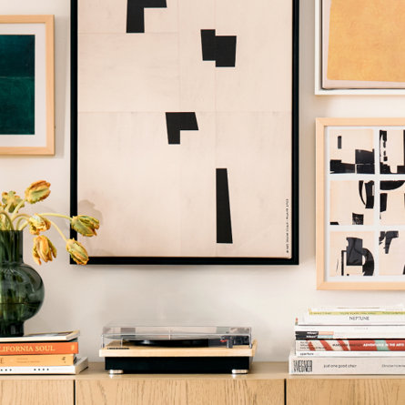Two framed geometric art prints above a table with a table lamp and a book
