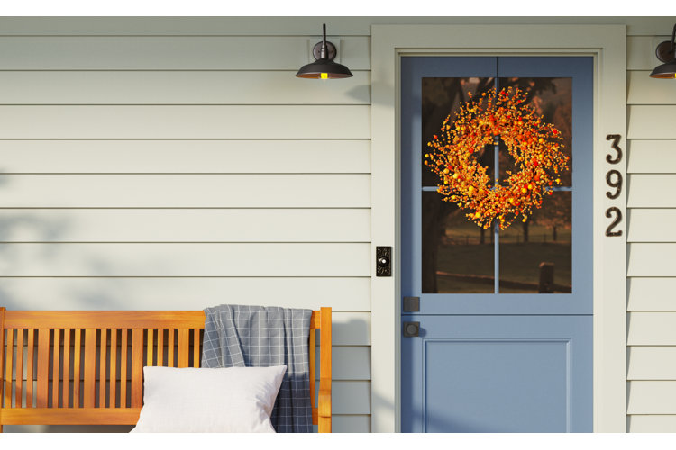 A front porch with a wooden bench and a blue door that's paired with an orange wreath.