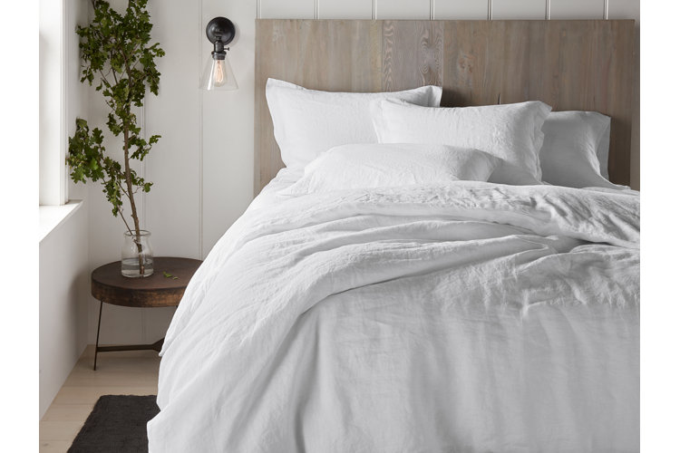 White linen duvet cover on a wooden bed and beside table with a green foliage arrangement.