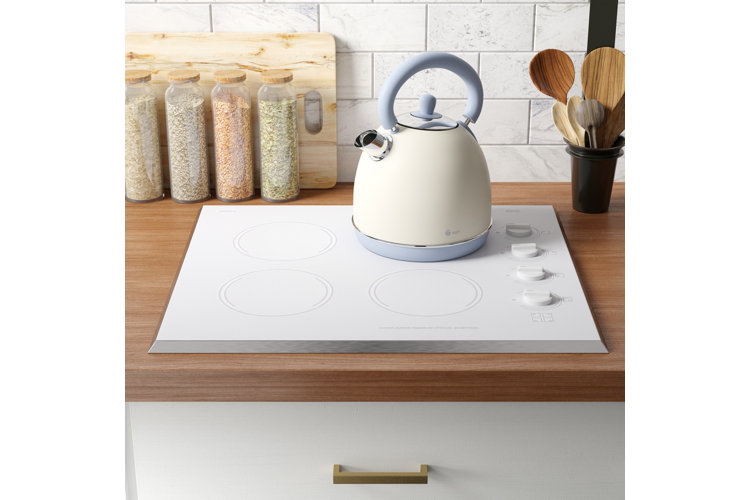 small white cooktop with a white kettle and a wood cutting board