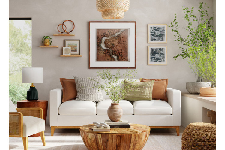 White living room with a framed painting of a desert canyon and river hanging above a white sofa with brown throw pillows.