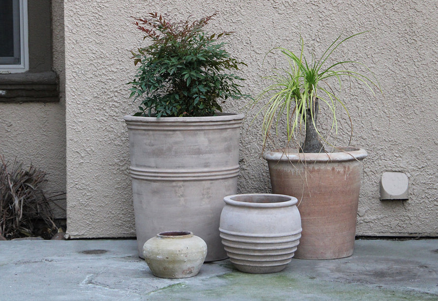 Group of terracotta planters filled with vibrant purple and red tulips sitting on a stone patio next to outdoor furniture.